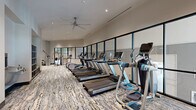 Located at 1133 West Baltimore Pike in Media, PA, this contemporary fitness center offers a generously sized, single-floor layout designed to accommodate a wide range of workout needs. The space is divided into distinct functional zones, each thoughtfully appointed to support a comprehensive fitness experience.

The cardio area features a row of modern treadmills, elliptical trainers, and additional aerobic machines positioned along a full-length wall of large, black-framed windows that flood the room with natural light and provide open views to the exterior. Overhead, industrial-style ceiling fans complement the recessed lighting, ensuring comfort throughout.

A dedicated strength training zone houses a variety of cable machines, functional trainers, and a dumbbell rack with wall-length mirrors, providing ample space for resistance-based workouts. Glass partition walls separate this area from the rest of the facility, maintaining an open, airy feel while defining each workout zone.

A separate studio space offers light wood flooring, spin bikes, a cable pull system, and ballet barres along mirrored walls, making it ideal for cycling classes, stretching, or barre-style training.

Throughout the facility, neutral-toned walls and patterned carpet tile flooring contribute to a clean, modern aesthetic. The high ceilings and expansive layout create a spacious, welcoming environment well-suited for a full-service fitness amenity.