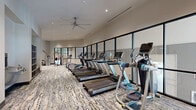 Located at 1133 West Baltimore Pike in Media, PA, this contemporary fitness center offers a generously sized, single-floor layout designed to accommodate a wide range of workout needs. The space is divided into distinct functional zones, each thoughtfully appointed to support a comprehensive fitness experience.

The cardio area features a row of modern treadmills, elliptical trainers, and additional aerobic machines positioned along a full-length wall of large, black-framed windows that flood the room with natural light and provide open views to the exterior. Overhead, industrial-style ceiling fans complement the recessed lighting, ensuring comfort throughout.

A dedicated strength training zone houses a variety of cable machines, functional trainers, and a dumbbell rack with wall-length mirrors, providing ample space for resistance-based workouts. Glass partition walls separate this area from the rest of the facility, maintaining an open, airy feel while defining each workout zone.

A separate studio space offers light wood flooring, spin bikes, a cable pull system, and ballet barres along mirrored walls, making it ideal for cycling classes, stretching, or barre-style training.

Throughout the facility, neutral-toned walls and patterned carpet tile flooring contribute to a clean, modern aesthetic. The high ceilings and expansive layout create a spacious, welcoming environment well-suited for a full-service fitness amenity.