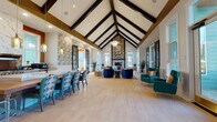 Located at 2200 Silver Crescent Dr in Charlotte, NC, this beautifully appointed single-floor gathering space showcases an impressive architectural design centered around dramatic vaulted ceilings with bold, dark exposed beams that draw the eye upward throughout the main hall. The expansive open-plan layout is anchored by a striking floor-to-ceiling fireplace clad in herringbone stonework and decorative patterned tile surround, topped with curated artwork that adds a lively focal point to the room.

Light hardwood-style flooring flows seamlessly throughout, complementing the bright, airy atmosphere created by oversized windows that invite abundant natural light. The living and lounge areas feature an eclectic mix of richly upholstered seating — including jewel-toned teal wingback chairs, navy velvet accent chairs, and a bold orange curved sofa — arranged to encourage conversation and relaxation.

The kitchen is a standout feature, equipped with professional-grade stainless steel appliances, a gas range, a marble-clad range hood, copper-toned brick backsplash, and light cabinetry topped with quartz countertops. Amber glass pendant lights add warmth above the communal dining table. Botanical-patterned wallpaper accents select walls, adding artistic character, while large glass-paned doors connect the space to the surrounding exterior.