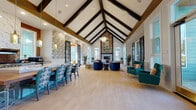 Located at 2200 Silver Crescent Dr in Charlotte, NC, this beautifully appointed single-floor gathering space showcases an impressive architectural design centered around dramatic vaulted ceilings with bold, dark exposed beams that draw the eye upward throughout the main hall. The expansive open-plan layout is anchored by a striking floor-to-ceiling fireplace clad in herringbone stonework and decorative patterned tile surround, topped with curated artwork that adds a lively focal point to the room.

Light hardwood-style flooring flows seamlessly throughout, complementing the bright, airy atmosphere created by oversized windows that invite abundant natural light. The living and lounge areas feature an eclectic mix of richly upholstered seating — including jewel-toned teal wingback chairs, navy velvet accent chairs, and a bold orange curved sofa — arranged to encourage conversation and relaxation.

The kitchen is a standout feature, equipped with professional-grade stainless steel appliances, a gas range, a marble-clad range hood, copper-toned brick backsplash, and light cabinetry topped with quartz countertops. Amber glass pendant lights add warmth above the communal dining table. Botanical-patterned wallpaper accents select walls, adding artistic character, while large glass-paned doors connect the space to the surrounding exterior.