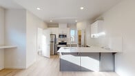 This contemporary three-floor home offers four bedrooms and three bathrooms across a well-organized layout. The main level features an open-concept living room bathed in natural light, with light-toned laminate flooring, recessed lighting, and sliding glass doors that lead to a balcony with outdoor views. A wall-mounted mini-split system ensures year-round comfort in this bright, airy space. The kitchen is a standout feature, showcasing white shaker cabinetry, stainless steel appliances including a range, microwave, and refrigerator, a white quartz island with a stainless sink, and a dedicated walk-in pantry for ample storage. A convenient bathroom is also accessible on this level. Carpeted staircases with wood railings connect the three floors, adding warmth to the transitions between levels. The bedrooms are generously proportioned, with the spacious primary suite offering a walk-in closet and plentiful natural light. Secondary bedrooms feature soft carpet flooring, recessed lighting, and windows overlooking the surroundings. The bathrooms are finished in a clean, modern style with gray vanity cabinetry, white countertops, sliding glass shower enclosures, and light wood-look flooring. Throughout the home, a neutral palette and consistent modern finishes create a cohesive, move-in-ready aesthetic.