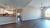 This single-floor residence offers a well-designed layout with a variety of functional spaces. The open living and dining area is finished with rich, dark hardwood-style flooring that extends throughout the main living spaces, complemented by neutral gray walls and clean white baseboards. A hallway connects the main area to additional rooms, with natural light filtering in through a window near the entry.

The kitchen is appointed with white cabinetry, dark granite-style countertops, and a full suite of stainless steel appliances, including a refrigerator, electric range, over-the-range microwave, and dishwasher. Track lighting illuminates the workspace effectively.

A standout bedroom features soaring ceilings, a ceiling fan with light fixture, and a striking arched window that floods the room with natural light and outdoor views. Additional bedrooms are carpeted and include ceiling fans, offering a comfortable and quiet atmosphere. A second carpeted bedroom also benefits from natural light via a window overlooking an exterior balcony railing.

The bathroom includes a tub-shower combination with white tile surround, a vanity with white cabinetry, and wood-style flooring. Storage is well-served by a generously sized walk-in closet outfitted with multi-tiered wire shelving and carpet underfoot.