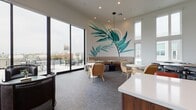 Located at 4000 Wilshire Boulevard in Los Angeles, this single-floor amenity lounge is a thoughtfully designed communal space that blends contemporary aesthetics with warm, inviting details. The interior is anchored by a striking large-scale tropical botanical mural rendered in vivid teal and green tones, creating an artistic focal point that sets the tone for the entire space.

The lounge area features a curved, channel-tufted banquette finished in neutral taupe, accompanied by marble-topped bistro tables with gold-accented bases and navy velvet ottomans, lending an upscale yet relaxed atmosphere. Rattan accent chairs and a sculptural circular pendant light add texture and visual interest throughout.

Floor-to-ceiling glass walls and sliding doors flood the space with natural light and open directly to an outdoor terrace with sweeping views of the surrounding Los Angeles skyline and palm-lined streetscape. A dedicated seating nook with a plush curved sofa and a cane-paneled accent chair takes full advantage of these panoramic views.

The kitchenette area is finished with rich walnut cabinetry, white quartz countertops, a chevron-patterned tile backsplash, floating wood shelves, and a row of statement bronze pendant lights overhead, completing this sophisticated and functional gathering space.