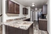 This two-floor residence offers a functional and cohesive interior design characterized by neutral wall tones, textured ceilings, and dark espresso-stained cabinetry that appears consistently throughout the space. The kitchen is well-appointed, featuring dark lower and upper cabinets with brushed nickel hardware, granite-look laminate countertops, a stainless steel double sink, and black appliances including a refrigerator, electric range, and dishwasher. Wood-look plank flooring runs through the kitchen and main living areas, lending warmth and visual continuity across the space.

The open living and dining area is illuminated by ceiling fans with integrated lighting and a small chandelier, contributing to a welcoming atmosphere. A dedicated entry door leads directly into the main living space. Bedroom areas include ceiling fans and a mix of wood-look flooring and plush carpeting, offering comfort underfoot. Windows allow natural light to filter in, enhancing the overall brightness of the rooms.

The bathroom is cleanly finished with a tub-shower combination, a dark-framed vanity mirror, dark cabinetry, and wood-look flooring. A dedicated laundry area houses a full-sized top-load washer and dryer with overhead shelving, adding significant practical value to the space.