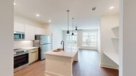 This well-designed 2-bedroom, 2-bathroom residence in Opelika, Alabama offers a thoughtful, modern layout across a single floor. The open-concept kitchen and living area serves as the heart of the home, anchored by a sleek white center island with a black matte faucet and pendant lighting above. The kitchen is equipped with stainless steel appliances, including a refrigerator and range, complemented by two-tone cabinetry featuring white uppers and warm wood-toned lowers, plus a herringbone tile backsplash. The living area extends naturally from the kitchen, bathed in natural light from large windows and a sliding glass door that opens to an outdoor space, with a ceiling fan adding comfort overhead. Warm wood-style flooring flows throughout the main living areas, while the bedrooms feature plush carpeting and ceiling fans. Each bedroom benefits from generous windows with outdoor views, providing a bright and airy atmosphere. The four closets offer ample storage throughout the unit. The bathroom showcases a tiled tub-surround with a subway tile pattern, matte black fixtures, and wood-style flooring. Additional conveniences include in-unit laundry, a pantry, and multiple closets, making this a highly functional and contemporary living space.
