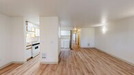 Located at 3000 SW Corbeth Ln in Troutdale, Oregon, this two-bedroom, one-bathroom single-floor home offers a practical and well-organized layout. Light wood laminate flooring runs throughout, lending warmth and visual continuity across every room. The open living and dining area is generously proportioned, filled with natural light from large windows that frame views of surrounding greenery, and is accessible via a sliding glass door that connects the interior to the outdoors. The galley-style kitchen features white cabinetry with wood-tone trim, laminate countertops, a stainless steel sink, and an electric range, with efficient use of space on both sides of the corridor. A dedicated laundry area is conveniently situated adjacent to the kitchen, housing a full-size washer and dryer. Both bedrooms are bright and comfortable, each equipped with sliding-door closets offering well-shelved storage space. The primary bedroom is notably spacious and includes access to additional closet areas. The full bathroom includes a wide vanity with ample under-sink storage and a large mirror. Four closets throughout the home provide exceptional storage capacity for a residence of this scale, making it a highly functional living space.