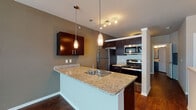 Located at 1806 Integrity Way in Louisville, Kentucky, this single-floor residence offers a well-appointed and contemporary living experience. The open-concept layout connects the living area to the kitchen, creating a cohesive and functional space throughout. Rich, dark hardwood flooring flows consistently across the main living areas, complementing the warm, neutral gray tones on the walls.

The kitchen is a standout feature, designed with dark espresso cabinetry, light granite countertops, and a full suite of stainless steel appliances including a refrigerator, electric range, and built-in microwave. A peninsula with an integrated sink and pendant lighting above serves as both a functional workspace and a natural divider between the kitchen and living area. Track lighting adds additional illumination to the cooking space.

The living area is generously proportioned, with windows allowing natural light to fill the room, creating a bright and welcoming atmosphere. The bathroom is clean and functional, featuring a tiled soaking tub and shower combination, dark vanity with granite countertop, and hardwood flooring. A dedicated laundry area includes a stacked washer and dryer unit alongside built-in shelving, providing practical in-unit convenience. Overall, the space presents a modern, well-designed interior suited for comfortable everyday living.