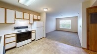 Located at 15510 W 63rd St in Shawnee, Kansas, this one-bedroom, one-bathroom unit offers a practical and well-organized layout across a single floor. The kitchen is equipped with white cabinetry featuring warm wood trim, a dishwasher, an electric range, a refrigerator, and ample counter space in an L-shaped configuration. Tile flooring runs throughout the kitchen, providing easy maintenance, while a flush overhead light fixture brightens the workspace. The open transition from the kitchen leads into the living area, which features plush carpeting and a window fitted with blinds that allows natural light to filter in. The bedroom is a comfortable, carpeted room with neutral walls, a window for natural light, and access to a closet with wood-paneled sliding doors. The bathroom includes a vanity with a light countertop, wood-trimmed cabinetry, and tile flooring, with a door connecting conveniently to the hallway. Warm wood baseboards and trim are consistent throughout the unit, lending a cohesive, classic aesthetic. The overall ambiance is clean, understated, and functional, making it a straightforward and efficient living space.
