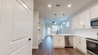 Located at 10951 Netherly Dr in Charlotte, NC, this well-designed single-floor, one-bedroom, one-bathroom home makes excellent use of its space through a thoughtful, open layout. The kitchen serves as a central highlight, featuring crisp white shaker cabinetry, light quartz countertops, a subway tile backsplash, and a full suite of stainless steel appliances including a refrigerator, range, microwave, and dishwasher. A peninsula with a undermount sink and pendant lighting above adds both functionality and style. Wood-look plank flooring runs throughout the main living areas, providing a warm, cohesive aesthetic. The living room is bright and welcoming, with multiple windows fitted with white blinds and a glass door that invites natural light and outdoor views. The bedroom is finished with plush carpet, a ceiling fan, and a well-sized window overlooking the exterior. The bathroom is cleanly appointed with white cabinetry, a light countertop, and wood-look flooring, with access to a walk-in closet featuring built-in shelving. Throughout the home, modern two-panel interior doors with matte black hardware add a clean, contemporary touch, tying together the neutral color palette and modern design elements.