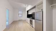 Located on Rue Sherbrooke Ouest in Montréal, this one-bedroom, one-bathroom unit offers a thoughtfully designed layout making efficient use of its compact footprint. Light-toned hardwood-style flooring runs throughout, lending a clean and cohesive aesthetic to the space.

The kitchen is a standout feature, outfitted with sleek white cabinetry, dark countertops, and a bold black tile backsplash that adds contrast and visual interest. Stainless steel appliances — including a full-size refrigerator, electric range with hood vent, and sink — provide full functionality. Open shelving above the refrigerator adds additional storage.

The living area adjoins the kitchen in an open-concept arrangement, benefiting from a window that brings in natural light. The bedroom is a well-proportioned private retreat with light-filled windows overlooking the surrounding streetscape, light hardwood-style flooring, and a sliding-door closet with built-in shelving and hanging space.

The bathroom is finished in classic white square tile on both the floors and walls, featuring a glass-enclosed walk-in shower, toilet, and a white vanity — creating a clean, bright atmosphere. Track lighting and a neutral white palette throughout the unit contribute to an overall modern and minimalist ambiance.