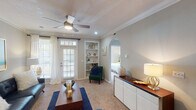 This single-floor residence offers a thoughtfully designed layout that balances comfort and functionality across its key living spaces. The living room serves as the heart of the home, featuring crown molding, a ceiling fan, soft carpet flooring, and large windows with sheer curtains that invite abundant natural light. A set of built-in shelves adds both character and practical storage, while an arched doorway connects seamlessly to the rest of the unit. The galley-style kitchen is outfitted with white cabinetry, dark granite countertops, a subway tile backsplash, stainless steel refrigerator, and light tile flooring, offering an efficient and clean workspace. The two bedrooms are generously sized, each with plush carpet, ceiling fans, and windows dressed with blinds and curtains. Both provide a comfortable, restful atmosphere with ample natural light. The two bathrooms mirror the kitchen's aesthetic, featuring matching dark granite vanity tops, white cabinetry, tile flooring, and shower-tub combinations with curtains. Crown molding and neutral wall tones carry throughout the space, contributing to a cohesive and polished overall ambiance.