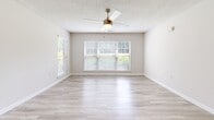 Located at 30 Grosslake Pkwy in Covington, GA, this well-appointed one-bedroom, one-bathroom unit offers a comfortable and functional layout across a single floor. The open-concept living and kitchen area is anchored by light hardwood-style flooring and neutral-toned walls, creating a bright and airy atmosphere. Large windows fitted with white blinds allow abundant natural light to fill the space, and ceiling fans in the main living area provide year-round comfort. The kitchen features crisp white cabinetry, light countertops with a peninsula breakfast bar, and black appliances including a range, dishwasher, and refrigerator — all flowing seamlessly into the living area. The spacious bedroom is carpeted for comfort, includes a ceiling fan, a window with outdoor views, and leads to a dedicated walk-in closet with built-in shelving. The bathroom is conveniently appointed, while a separate laundry room houses a full-size Whirlpool top-load washer and dryer alongside a utility shelf and window. Textured ceilings and clean white trim throughout lend a consistent, polished finish to this thoughtfully designed home in Covington, Georgia.