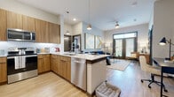 This contemporary single-floor residence offers a thoughtfully designed open-concept layout that seamlessly connects the kitchen, dining, and living areas. The kitchen is a standout feature, outfitted with warm wood cabinetry, quartz countertops, stainless steel appliances including a full-size refrigerator, range, microwave, and dishwasher, complemented by pendant lighting and light wood-style flooring. The kitchen flows naturally into the living area, which benefits from a ceiling fan, large windows, and access to an outdoor space, filling the room with natural light.

The living space provides a comfortable, modern ambiance, highlighted by bold décor and stylish finishes. Two bedrooms offer plush carpeting, large windows with ample natural light, and direct access to their respective bathrooms. The primary bathroom features a dual-sink vanity with wood cabinetry, a soaking tub, light wood-style flooring, and a walk-in closet. The second bathroom mirrors the clean, modern aesthetic with a tub-shower combination, wood vanity, and an adjacent walk-in closet. Throughout the residence, dark-framed door accents and neutral tones create a cohesive, contemporary design aesthetic.