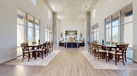 Located at 975 14th St in Oroville, California, this single-floor community space offers a generously proportioned, open-concept layout designed for both comfort and functionality. The interior is immediately defined by its dramatic double-height ceilings, which create an expansive, airy atmosphere throughout the entire floor plan.

The living area is furnished with charcoal leather seating accented by vibrant yellow throw pillows, arranged around a wooden coffee table to create an inviting lounge environment. Lush potted greenery adds warmth and a natural touch to the contemporary décor. Floor-to-ceiling glass wall panels and large aluminum-framed windows flood the space with abundant natural light while offering clear sightlines to the outdoor pool and surrounding grounds.

The dining area features a solid wood table with cross-back chairs set atop a neutral area rug, positioned to take full advantage of the panoramic window views. Glass panel doors provide seamless indoor-outdoor connectivity, opening directly to the pool terrace.

Throughout the space, light-toned hardwood-style flooring ties the living and dining zones together cohesively. The neutral gray wall palette, clean architectural lines, and modern fixtures contribute to a polished yet welcoming atmosphere. A kitchenette area is visible in the background, enhancing the space's versatility for gatherings and community events.