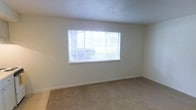 This single-story space presents a clean, straightforward layout designed for comfortable living. The room visible in the image is finished with wall-to-wall beige carpeting, which adds a soft, neutral foundation to the interior. Smooth white walls and a white ceiling contribute to a bright, open atmosphere throughout the space.

A prominent feature of the room is the large window fitted with horizontal blinds, which allows an abundance of natural light to filter in while maintaining privacy. The window frames views of outdoor greenery, bringing a connection to the outside environment. The window's size ensures the room feels airy and well-lit throughout the day.

The walls are clean and unadorned, providing a blank canvas adaptable to a variety of interior arrangements and décor styles. White baseboards line the perimeter of the room, offering a crisp contrast to the carpeted floor. The overall ambiance is calm and neutral, making the space versatile and move-in ready. The single-floor layout offers convenience and accessibility, with a straightforward design that prioritizes functional living.