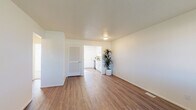 This single-floor unit offers a clean, functional layout designed with a neutral aesthetic throughout. The living area is open and airy, featuring wood-look laminate flooring, white walls, and a louvered closet door, with a clear sightline into the kitchen beyond. A second living or flex space provides additional room, finished with darker wood-look flooring and a wide window that allows natural light to fill the area.

The kitchen is a standout feature, outfitted with crisp white shaker cabinetry, brushed nickel hardware, a classic white subway tile backsplash, a stainless steel double-basin sink, and stainless steel appliances including a range and dishwasher. A narrow sidelight window beside the exterior door brings in additional natural light, enhancing the kitchen's bright, contemporary feel.

The bedrooms are carpeted and individually windowed, offering views of surrounding greenery. Each room maintains the unit's consistent white walls and simple, functional character. The bathroom is straightforwardly appointed with a white vanity, wood-look flooring, and a tub-shower combination. Throughout the unit, floor vents indicate a central HVAC system, contributing to a comfortable and efficiently designed living environment.