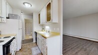 This single-floor unit is thoughtfully laid out across several distinct areas, each with its own character and function. The galley-style kitchen is efficiently organized, featuring white cabinetry with decorative wire-mesh upper doors, granite-look countertops, a stainless steel sink, and white appliances including an electric range and refrigerator. Durable wood-look vinyl plank flooring runs throughout the kitchen and connects seamlessly to the adjoining living spaces.

The open living area is bright and spacious, benefiting from a large sliding glass door that floods the room with natural light and provides access to an outdoor space. The neutral-toned walls, textured ceiling, and gray-toned vinyl plank flooring give the room a clean, versatile aesthetic. A baseboard heating unit runs along one wall. A secondary open area near the entryway features a built-in closet with louvered doors, offering convenient storage.

The bedroom is a calm, private retreat with soft carpeting, warm neutral walls, a textured ceiling, a window with blinds, and a baseboard heater. The bathroom includes a vanity with a decorative cabinet, a stone-patterned countertop, an undermount sink, and classic white tile wall surround, completing the unit with a timeless, functional finish.