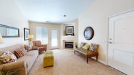 This single-floor residence offers a well-organized layout with distinct living, dining, sleeping, and utility spaces. The living room is a standout area, centered around a corner fireplace with a white mantel and framed by neutral-toned walls and plush carpeting. A set of glass-paned doors introduces natural light and provides exterior access, complementing the room's open, comfortable feel. A wall-mounted mirror and framed artwork add visual interest throughout.

The galley-style kitchen features wood-trimmed cabinetry, tile flooring, a double sink, dishwasher, electric range, and refrigerator, with a skylight overhead that brightens the compact workspace. Adjacent to the kitchen, the dining area accommodates a full-sized table and chairs beneath decorative wall art, creating a defined yet connected eating space.

Both bedrooms are carpeted and offer natural light through windows. The primary bedroom features an arched window, providing an architectural accent, while the second bedroom includes ample room for a dresser and sitting chair. The full bathroom includes a tub-shower combo with tile surround and tile flooring. A dedicated laundry room houses a full-sized washer and dryer alongside a water heater, providing practical in-unit utility space.