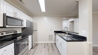 This efficiently designed 1-bedroom, 1-bathroom residence offers a thoughtful layout across a single floor, encompassing a combined dining, kitchen, and living area, a dedicated dining room, hallway, bedroom, bathroom, and closet. The kitchen is a standout feature, showcasing white shaker-style cabinetry, dark granite countertops, and a full suite of stainless steel appliances including a refrigerator, range, built-in microwave, and dishwasher. A double-basin sink with a modern gooseneck faucet anchors the countertop peninsula, and crown molding adds a refined touch overhead. Light wood-look luxury vinyl plank flooring runs consistently throughout the unit, creating a cohesive and easy-to-maintain aesthetic. The bedroom offers a comfortable footprint, a ceiling fan with lighting, a window with blinds that allows in natural light, and access to a closet. The hallway features chair-rail molding detail along the walls, lending a classic character to the entryway. The bathroom includes a white vanity with dark granite countertop, a tub/shower combination, and matching flooring. Neutral warm-gray walls throughout provide a clean, versatile backdrop, making this a well-balanced and move-in-ready space.