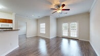 This single-floor residence offers a clean, functional layout with consistent hardwood-style flooring flowing throughout the space, creating a cohesive and polished look from room to room. The living area is a standout feature, highlighted by elegant crown molding, a ceiling fan with a light fixture, and a set of French doors that invite natural light and provide outdoor access. An additional window further brightens the room, contributing to an open and airy atmosphere. The kitchen is designed for practicality, featuring rich warm-toned cabinetry, granite-style countertops, a double sink, and white appliances including a range, refrigerator, and overhead microwave. A closet door within the kitchen provides convenient pantry or storage space. The bathroom is accessible via a hallway flanked by closets, offering ample built-in storage. The vanity area features white cabinetry, a large mirror, and a well-lit fixture above. A separate wet area includes a full soaking tub surrounded by classic white tile. The bedrooms are comfortably sized with neutral walls, hardwood-style flooring, and windows fitted with blinds that allow for natural light and privacy. Overall, the space presents a tidy, move-in-ready environment with practical finishes and a welcoming ambiance throughout.