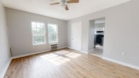 Located at 425 W Tennessee St in Florence, Alabama, this single-floor loft unit offers a clean, functional layout with a refreshed, modern aesthetic. The main living area is a standout feature, showcasing light-toned hardwood flooring that reflects abundant natural light streaming in through large, multi-pane windows. Soft gray walls and crisp white trim create a neutral, welcoming atmosphere, while a ceiling fan overhead adds both style and practicality. A closet and open passageway connect the living space to the rest of the unit seamlessly. The kitchen is well-appointed with white shaker-style cabinetry, warm-toned countertops, and stainless steel appliances including a refrigerator and range. Light ceramic tile flooring and a window above the sink keep the space bright and easy to maintain. The bathroom continues the clean aesthetic with full white subway tile surrounding a soaking tub, complemented by a natural light source from a window. Throughout the unit, consistent neutral tones, white doors with classic paneling, and hardwood flooring tie the spaces together cohesively. This loft offers a practical and comfortable living environment in a convenient Florence location.
