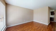 This single-floor unit offers two bedrooms and two full bathrooms within a well-organized layout. A hallway with warm wood-look flooring and neutral beige walls connects the main living areas, with a wall-mounted HVAC unit and convenient access to the front entry, which benefits from natural light through a sidelight window.

The living and common areas feature rich, warm-toned wood-look flooring throughout, complemented by clean white baseboards and a neutral color palette that lends a bright, open feel. The kitchen is equipped with dark espresso cabinetry, light countertops, a black electric range, an under-cabinet range hood, and a double-basin stainless steel sink positioned beneath a window for natural light.

Both bedrooms are carpeted and feature ceiling fans with light fixtures, windows with blinds for natural light and privacy, and access to closet space. The rooms maintain a consistent neutral tone throughout.

The two bathrooms each include a tub-shower combination with white surrounds, wood-look flooring, vanity cabinetry, and a toilet, providing functional and clean full bath accommodations. Overall, the unit presents a practical and cohesive design.