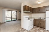 This single-floor residence offers a practical and comfortable layout across several well-defined living areas. The living room serves as the heart of the home, highlighted by a stone-faced fireplace and large sliding glass doors that open to a private balcony with outdoor views of surrounding trees, filling the space with natural light. Carpet flooring and a wall-mounted air conditioning unit complete this welcoming area. Adjacent to the living room, the kitchen is equipped with dark wood cabinetry, a coil-top electric range, a refrigerator, a sink, and a ventilation hood. Tile flooring and wood-paneled wainscoting add a classic character to this functional space, which also connects to a dining area featuring a ceiling fan. The bedroom is generously sized, with carpet flooring, a ceiling fan, a window with natural light, and access to a spacious walk-in closet outfitted with dual wire shelving systems for ample storage. The full bathroom includes a soaking tub with white tile surround, a vanity with cabinet storage, a medicine cabinet mirror, and tile flooring. Throughout the residence, textured ceilings, baseboard heating, and warm-toned wood accents contribute to a cohesive and functional aesthetic.
