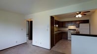 Located at 603 S Main St in Fond du Lac, Wisconsin, this single-floor residence offers a practical and comfortable layout designed for everyday living. The open-concept design connects the carpeted living area to the kitchen, creating a sense of continuity throughout the main living space. The kitchen is well-appointed with rich, dark wood cabinetry that provides ample storage, a built-in sink, white electric range, and under-cabinet lighting that adds warmth to the cooking area. The tile flooring in the kitchen contrasts nicely with the plush carpeting in the adjacent living space, clearly delineating the two functional zones. A ceiling fan is visible overhead, contributing to air circulation and comfort throughout the unit. The neutral, light-colored walls throughout keep the space feeling bright and open. A hallway visible from the main living area leads to additional rooms, suggesting a thoughtful floor plan that separates the living and private spaces. Baseboard heating units are present along the walls, ensuring comfortable temperatures year-round. This straightforward, move-in-ready residence offers a clean and functional environment well-suited for those seeking a low-maintenance living space in Fond du Lac.