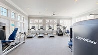Located at 5150 Jack Byrnes Dr in Murfreesboro, Tennessee, this fitness center offers a bright, well-appointed space designed to support a comprehensive workout experience. The single-floor facility is finished with neutral gray carpeting and crisp white crown molding, lending the space a clean, polished aesthetic that feels both functional and inviting.

Large multi-pane windows line the walls on multiple sides, flooding the interior with abundant natural light and providing views of the surrounding neighborhood. Recessed ceiling lighting and a ceiling fan ensure the space remains well-lit and comfortable during any time of day or season.

The cardio area is generously stocked with a row of Life Fitness treadmills, an elliptical trainer, a stair climber, and a recumbent bike, all equipped with modern digital displays. The strength training section features multiple Life Fitness selectorized cable and weight machines with blue upholstery, accommodating a wide range of resistance exercises. A dedicated free weights and functional training area includes kettlebells, medicine balls in various sizes, resistance bands, and step platforms neatly organized on a rack.

Framed wall mirrors are positioned throughout the space to allow users to monitor their form. A warm-toned wood door provides access to an adjacent area, adding a classic architectural touch. Overall, this fitness center offers a comprehensive, thoughtfully arranged environment suited for residents seeking convenient, high-quality exercise amenities.