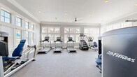 Located at 5150 Jack Byrnes Dr in Murfreesboro, Tennessee, this fitness center offers a bright, well-appointed space designed to support a comprehensive workout experience. The single-floor facility is finished with neutral gray carpeting and crisp white crown molding, lending the space a clean, polished aesthetic that feels both functional and inviting.

Large multi-pane windows line the walls on multiple sides, flooding the interior with abundant natural light and providing views of the surrounding neighborhood. Recessed ceiling lighting and a ceiling fan ensure the space remains well-lit and comfortable during any time of day or season.

The cardio area is generously stocked with a row of Life Fitness treadmills, an elliptical trainer, a stair climber, and a recumbent bike, all equipped with modern digital displays. The strength training section features multiple Life Fitness selectorized cable and weight machines with blue upholstery, accommodating a wide range of resistance exercises. A dedicated free weights and functional training area includes kettlebells, medicine balls in various sizes, resistance bands, and step platforms neatly organized on a rack.

Framed wall mirrors are positioned throughout the space to allow users to monitor their form. A warm-toned wood door provides access to an adjacent area, adding a classic architectural touch. Overall, this fitness center offers a comprehensive, thoughtfully arranged environment suited for residents seeking convenient, high-quality exercise amenities.