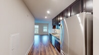 This single-floor residence offers a thoughtfully designed layout that balances functionality and style. The galley-style kitchen is a standout feature, equipped with rich dark cabinetry that extends to the ceiling, light granite countertops, a stainless steel sink, and a full suite of stainless steel appliances including a refrigerator, range, microwave, and dishwasher. Recessed lighting illuminates the space, which flows seamlessly into the living area. The living room is bright and open, featuring warm hardwood-style flooring, neutral walls, and a glass door with access to a private balcony that invites natural light. A ceiling-mounted HVAC unit provides efficient climate control. The bathroom is classically designed with a black-and-white penny tile floor, a combined shower and soaking tub with white subway tile surround, and a vanity with a white countertop and sleek hardware. The unit also includes a dedicated laundry area with a full-size stacked washer and dryer and built-in wire shelving for additional storage. Consistent hardwood-style flooring runs throughout, tying each space together with a clean, modern aesthetic.