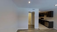 This studio is a well-organized, single-floor unit that makes smart use of its compact footprint. The open-plan layout seamlessly connects the living area to the kitchen, creating a cohesive and functional living environment. The kitchen is equipped with dark cabinetry, black appliances including a range and over-the-range microwave, and a sink with ample counter space — offering a practical setup for everyday cooking. Wood-style plank flooring runs throughout the main living area, adding warmth and a modern aesthetic to the space. The clean, white walls are paired with recessed lighting, contributing to a bright and airy atmosphere. A dedicated bathroom is accessible directly from the main living space, featuring tile flooring and standard fixtures. HVAC ventilation is present overhead, ensuring climate control throughout the unit. The overall design is straightforward and move-in ready, with a neutral color palette that allows for personalization. This studio is an ideal option for those seeking a low-maintenance, efficiently laid-out living space.