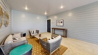 Located at 2007 Knoll Top Ln in Franklin, Tennessee, this single-floor living space offers a cohesive and thoughtfully designed interior with a relaxed yet refined aesthetic. The room is defined by floor-to-ceiling shiplap walls in a soft gray-white finish, lending a clean, contemporary farmhouse character throughout.

The space is organized into two functional zones. A casual lounge area features woven rattan-style seating, including a sofa, accent chairs, and a coffee table, all anchored by a warm geometric-patterned area rug. Decorative woven wall art and framed prints contribute to the curated, coastal-inspired ambiance. A slim console table runs along one wall, adding both style and utility.

A dining area occupies the opposite end, centered around a modern rectangular table with wire-frame chairs and a bold black and white striped runner. A vibrant abstract artwork adorns the shiplap wall behind it, adding an artistic focal point.

Recessed lighting throughout the ceiling provides even, warm illumination, while a large opening at one end of the room floods the space with natural light and offers a view to the outdoors, enhancing the airy, open feel. Polished concrete floors tie the entire space together with a sleek, durable finish that complements the room's modern-rustic tone.