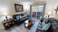 This single-floor residence offers a thoughtfully designed layout across several distinct living areas. The living room serves as the heart of the home, featuring light wood-style flooring, a textured ceiling, and large sliding glass doors that flood the space with natural light and open onto a private balcony. The kitchen is efficiently laid out with white cabinetry, granite-look countertops, and a full suite of white appliances including a range, microwave, and refrigerator, complemented by wood-style flooring that continues the cohesive aesthetic. Adjacent to the living area, the dining space includes a ceiling fan and offers a cozy setting for meals. The bedroom is carpeted for comfort and includes direct balcony access through sliding glass doors, a walk-in closet, and ample room for a full furniture arrangement. Two bathrooms serve the residence; both feature granite-look countertops, white cabinetry, and tub-shower combinations. The primary bathroom includes a wide vanity with a large mirror and bright overhead lighting. Warm neutral wall tones carry throughout the entire residence, creating a cohesive and welcoming ambiance from room to room.