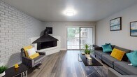 This two-floor residence offers a thoughtfully designed layout with modern finishes throughout. The entryway opens to a view of both the kitchen and the main living area, establishing a connected, open feel. The kitchen is well-appointed with white shaker-style cabinetry, gray stone countertops, a classic subway tile backsplash, and a full suite of stainless steel appliances including a range, microwave, and refrigerator. Rich wood-look flooring runs throughout the main living spaces, adding warmth and continuity. The living room is a standout area, anchored by a distinctive corner brick fireplace and flooded with natural light through sliding glass doors that open to an outdoor space with lush greenery views. The primary bedroom also features sliding glass doors overlooking a landscaped courtyard, complemented by an accent brick wall that adds character. Additional bedrooms are comfortably sized with natural light from windows. The bathrooms include a full bath with a subway tile tub surround and a half bath finished with marble-look tile flooring and a corner vanity. Neutral gray tones and clean white trim are carried consistently throughout, creating a cohesive, contemporary aesthetic across both floors.