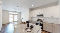 Located at 255 Williamsburg Pkwy in Fate, TX, this well-appointed single-floor unit offers a thoughtfully designed layout that maximizes functionality. The open-concept kitchen and living area serves as the heart of the space, featuring a large granite-topped island with an undermount sink, two-tone cabinetry with white upper and warm taupe lower cabinets, a classic subway tile backsplash, and a full suite of stainless steel appliances including a side-by-side refrigerator, electric range, over-the-range microwave, and dishwasher. Recessed lighting and a ceiling fan keep the space bright and comfortable, while a glass-panel entry door allows natural light to flow in. Rich wood-look flooring runs consistently throughout the unit, lending warmth and visual continuity. The bedroom offers a ceiling fan, a window with a view of the outdoor pool area, and access to a spacious walk-in closet with multi-tier shelving and hanging rods. A second closet provides additional storage. The full bathroom is finished with a granite-topped vanity, a large mirror, wood-look flooring, and a tiled tub-shower combination. A dedicated laundry area completes this efficiently organized and modern single-floor residence.