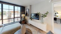 Located at 33 N St NE in Washington, DC, this contemporary single-floor residence showcases a thoughtfully designed open-concept layout with modern finishes throughout. The kitchen is a standout feature, equipped with stainless steel appliances including a bottom-freezer refrigerator, gas range, built-in microwave, and dishwasher. Two-tone cabinetry pairs crisp white upper cabinets with warm wood-grain lower cabinets, complemented by a light tile backsplash and a freestanding kitchen island with a white quartz top. Light-toned hardwood flooring flows seamlessly throughout the main living areas. The living room benefits from large, steel-framed windows that flood the space with natural light and offer open urban views of the surrounding Washington, DC neighborhood. A bold dark accent wall adds contrast and depth to the living area. The bedroom features generous natural light through similarly styled steel-framed windows, plush carpeting, and ample space for a full furniture arrangement. The bathroom includes large-format tile flooring, a full soaking tub with shower, and a wood-accented vanity with a clean white countertop. A walk-in closet is directly accessible from the bathroom, providing practical and well-organized storage. Track lighting is used throughout, enhancing the modern, urban aesthetic of the overall space.