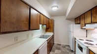 This single-story unit at Premier offers a practical and straightforward layout across several well-defined spaces. The galley-style kitchen is efficiently organized, featuring warm-toned wood cabinetry lining both walls, white countertops, a double-basin stainless steel sink, and white appliances including a refrigerator, electric range, and dishwasher. Stone-patterned tile flooring runs throughout the kitchen, adding a durable and easy-to-maintain surface underfoot.

The living area is generously proportioned, finished with wall-to-wall carpet and neutral painted walls that create a clean, versatile backdrop. A large sliding glass door dressed with vertical blinds fills the space with natural light and provides views of the surrounding greenery, along with direct access to an outdoor area. A dedicated HVAC vent and thermostat keep the space climate-controlled year-round.

The bedroom continues the carpeted flooring and features a window with blinds that allows natural light to filter in while maintaining privacy. The bathroom is appointed with a full-size soaking tub and shower combination, chrome fixtures, and a built-in shelf niche, finished with clean white surrounds. Overall, the unit presents a functional and comfortable living environment with a consistent, neutral aesthetic throughout.