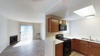 Located at 525 E Camden Ave in El Cajon, this single-floor unit offers a functional and open layout that connects the kitchen and living areas seamlessly. The kitchen is equipped with warm medium-toned wood cabinetry, a black electric range, and a built-in microwave above the stove. Light-colored countertops provide ample prep space, and a skylight overhead floods the kitchen with natural daylight, enhancing the bright, airy feel of the space. The cabinetry offers generous storage with upper and lower cabinet configurations. The living area extends naturally from the kitchen, featuring wood-style flooring that runs throughout and large sliding glass doors dressed with sheer curtains, allowing abundant natural light to fill the room. A wall-mounted air conditioning unit ensures year-round comfort. The sliding doors open to an outdoor space, providing a connection to the exterior. The overall ambiance of the unit is clean, practical, and well-lit, making it a comfortable and straightforward living space suited for everyday functionality.