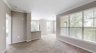 Located at 465 Elmcroft Blvd in Rockville, MD, this sophisticated single-floor community space offers a seamlessly connected living room, dining area, and kitchen across a generously sized open layout. The interior is immediately distinguished by striking coffered ceilings accented in teal, framed by crisp white molding that adds architectural depth and elegance throughout. Underfoot, a classic herringbone-patterned wood-look floor flows uniformly across the entire space, enhancing the sense of continuity and refined design. The living room is anchored by a white fireplace with a built-in bookshelf and media wall, complemented by teal upholstered seating and abundant natural light pouring in through floor-to-ceiling windows that offer views of an outdoor pool and patio area. Sheer drapery softens the light while maintaining the bright, airy ambiance. The kitchen features a large island with a crisp white countertop and navy blue base, surrounded by upholstered bar seating, white cabinetry, and integrated appliances. The dining area transitions naturally from the kitchen, creating a functional and stylish entertaining hub. Recessed lighting and thoughtfully placed wall art complete the polished, welcoming atmosphere of this beautifully appointed space.