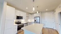 This well-appointed 660 square foot, single-floor apartment offers a thoughtfully designed layout that maximizes space and functionality. The open-concept kitchen is a standout feature, showcasing white shaker cabinetry, a subway tile backsplash, stainless steel appliances including a French door refrigerator, electric range, and built-in microwave, as well as a large center island with a quartz countertop illuminated by pendant lighting — ideal for both meal prep and casual dining. A stacked washer and dryer unit is conveniently tucked within a dedicated closet off the kitchen area. Light hardwood flooring flows seamlessly throughout the entire unit, enhancing the bright and airy atmosphere created by neutral wall tones. The 150 square foot primary bedroom is a comfortable retreat, equipped with a ceiling fan and access to both a private bathroom and a walk-in closet outfitted with double-tier wire shelving for ample storage. The bedroom is further brightened by a large window offering views of the surrounding neighborhood. A private balcony extends the living space outdoors. The unit's clean, modern aesthetic and efficient floor plan make it an ideal urban living space.