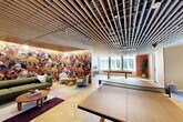 Located at 1070 Bridgeview Way in San Francisco's vibrant Mission Bay neighborhood, this amenity lounge is a thoughtfully designed communal space that blends sophisticated aesthetics with recreational functionality. The single-floor layout is unified by a dramatic slatted wood ceiling that runs throughout, adding warmth and architectural depth to the open, airy environment.

The main area serves as a multi-use gathering space, anchored by a full-size ping pong table and a billiards table positioned near floor-to-ceiling windows that invite abundant natural light and views of the surrounding urban landscape. A statement wall mural — richly illustrated with vivid, nature-inspired imagery in warm autumnal tones — commands attention and adds an artistic focal point to the lounge area, where contemporary seating arrangements encourage casual conversation and relaxation.

Herringbone-patterned hardwood flooring flows seamlessly throughout the space, grounding the design with classic elegance. Semi-private nook areas are tucked thoughtfully within the layout, each outfitted with sectional sofas, accent lighting, and curated artwork, offering more intimate settings within the broader open plan. Steel-framed glass partitions provide subtle visual separation while preserving the sense of openness. The overall ambiance is modern, inviting, and well-appointed — ideal for both social gatherings and leisurely downtime.