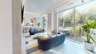 Located at 610 Martin Grove Rd in Toronto, Ontario, this contemporary single-floor space offers a thoughtfully designed layout comprising a living room and dining room. The interior is defined by a clean, modern aesthetic, with crisp white walls, light tile flooring, and warm wood-toned cabinetry and accent panels that add natural warmth throughout.

The living room is a bright and inviting space anchored by plush navy-blue sofas adorned with colourful accent cushions, arranged atop a bold striped area rug. Floor-to-ceiling glazed sliding doors flood the room with natural light and offer direct views of a lush, green outdoor area, creating a seamless indoor-outdoor connection. A decorative slatted accent wall with circular mirror sconces and a wall-mounted television add character and functionality to the space.

The dining area features a large, light-toned communal table surrounded by striking burnt-orange upholstered chairs, set against a backdrop of sleek wood cabinetry and a subtle wet bar. Recessed ceiling lighting with warm cove accents creates an inviting ambiance. Together, the two areas flow cohesively, making this a versatile and welcoming space ideal for gathering and socializing.