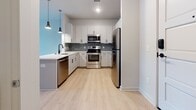 Located at 5000 Libbie Mill East Blvd in Richmond, Virginia, this single-floor residence offers a thoughtfully designed open-concept layout with clean, contemporary finishes throughout. Light hardwood-style flooring runs continuously across the living, dining, and bedroom areas, lending a sense of warmth and cohesion to the entire space.

The open living area is bright and welcoming, with large windows fitted with horizontal blinds that allow natural light to filter in while maintaining privacy. The space flows seamlessly into the kitchen, which is well-appointed with white shaker-style cabinetry, a subway tile backsplash, stainless steel appliances including a refrigerator, range, microwave, and dishwasher, and a light countertop peninsula with stylish pendant lighting overhead.

The bedroom features generous proportions, multiple windows offering views of the surrounding community, and direct access to a walk-in closet with built-in shelving. The bathroom is finished with large-format neutral tile flooring, a vanity with ample storage, and a full tub-shower combination, maintaining the clean and modern aesthetic found throughout the residence.

Neutral wall tones, recessed lighting, and consistent modern hardware tie the space together, creating a functional and visually cohesive living environment in the heart of the Libbie Mill neighborhood.