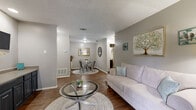 Located at 2355 Austin Highway in San Antonio, TX, this single-story 1-bedroom, 2-bathroom residence offers a thoughtfully designed layout that maximizes every square foot. The open living and dining area is anchored by rich hardwood-style flooring, neutral gray walls, and a textured ceiling, creating a warm and cohesive atmosphere. A sliding glass door in the living room fills the space with natural light and provides direct access to a private patio with outdoor views. The galley-style kitchen features dark cabinetry, light countertops, black appliances, and a window that brings in additional natural light. The dining area flows seamlessly from the kitchen and living space, making entertaining easy. The bedroom is carpeted for comfort, features a ceiling fan with light, and benefits from natural light through well-dressed windows. Three closets, including a spacious walk-in, provide ample storage throughout. The two bathrooms include one with a full tub-shower combination with white tile surround, and another with a wide vanity featuring dark cabinetry and a large mirror. This residence offers a practical and inviting layout suited for comfortable everyday living in San Antonio.