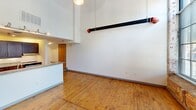 This two-story loft in Charlotte's vibrant 28205 neighborhood blends industrial character with modern comfort. The main level showcases soaring ceilings with exposed piping, rich hardwood floors, and a striking open living area anchored by large arched windows set in original brick walls that flood the space with natural light. The kitchen features dark wood cabinetry, granite countertops, and stainless steel appliances. A staircase connects both floors, where two bedrooms offer hardwood flooring and accessible bathrooms with clean, modern fixtures. The second bedroom features clerestory windows and a slatted wood ceiling, adding architectural interest throughout.