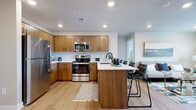 This thoughtfully designed two-bedroom, two-bathroom residence in Sterling Heights, Michigan offers a well-appointed single-floor layout with modern finishes throughout. The open-concept living area features neutral-toned walls, recessed lighting, and light hardwood-style flooring that flows seamlessly through the main living spaces. A large window in the living room allows natural light to fill the room, creating a bright and welcoming atmosphere.

The kitchen is a standout feature, showcasing warm wood-grain cabinetry with matte black hardware, crisp white quartz countertops, and a full suite of stainless steel appliances including a refrigerator, electric range, built-in microwave, and dishwasher. A peninsula with bar seating connects the kitchen to the living area, reinforcing the open layout and providing additional dining space.

Both bedrooms are comfortably sized, with plush carpeting and windows that bring in natural light. The bathrooms are finished with wood-toned vanities, white quartz counters, and a tub-shower combination with a sleek black-framed sliding glass door. A dedicated laundry area houses a stacked washer and dryer unit, adding everyday convenience to this well-rounded residence.