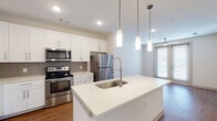 Located at 2007 Knoll Top Ln in Franklin, Tennessee, this single-floor residence offers a clean, modern aesthetic with thoughtfully designed living spaces. The open-concept kitchen serves as the centerpiece of the home, showcasing crisp white shaker cabinetry, a gray subway tile backsplash, and a full suite of stainless steel appliances including a range, over-the-range microwave, and refrigerator. A generously sized island with a white quartz countertop and undermount sink provides both prep space and casual seating, illuminated overhead by stylish cylindrical pendant lights. Warm hardwood-style flooring extends throughout the main living areas, complementing the neutral white walls and creating a cohesive, inviting atmosphere. The living area is brightened by natural light streaming through large windows fitted with horizontal blinds. The bathroom features a full soaking tub and shower combination with built-in shelving and brushed nickel fixtures set against clean white surrounds. A dedicated laundry room houses a full-size top-loading washer and dryer side by side, complete with overhead wire shelving for added storage. Additional rooms offer flexible space with ample natural light and views to the outdoors, making this a well-appointed and functional residence in the heart of Franklin, TN.