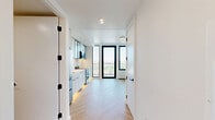 Located at 104 Fleet Pl in Brooklyn, NY, this thoughtfully designed one-bedroom, one-bathroom residence offers a clean, modern aesthetic throughout its efficiently utilized single floor. Elegant herringbone-patterned hardwood flooring runs seamlessly through the living areas and bedroom, lending warmth and a sophisticated visual rhythm to the space.

The kitchen is a standout feature, designed as a streamlined galley with sleek white cabinetry — including glass-front upper cabinets with dark trim accents — paired with a white quartz countertop and under-cabinet accent lighting. Stainless steel appliances, including a refrigerator, electric range, and built-in microwave, complete the contemporary setup. A floor-to-ceiling window with a matte black frame floods the kitchen with natural light and offers sweeping city views.

The bedroom is a calm, minimalist retreat with bright white walls and the same herringbone flooring, creating a clean and airy feel.

The bathroom is finished to a high standard, featuring terrazzo-style flooring, vertical mosaic tile surrounding the soaking tub and shower combination, a warm wood-toned vanity with an integrated white sink, and recessed lighting. Matte black hardware details throughout tie the design together cohesively, reflecting the modern sensibility found across the entire residence.
