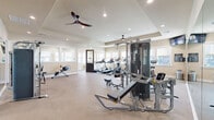 Located at 1420 S Tyler Ave in Loveland, Colorado, this single-floor amenity facility offers a thoughtfully designed layout encompassing a comprehensive range of functional spaces. The layout is anchored by a spacious, light-filled exercise room featuring an impressive array of fitness equipment, including cable machines, treadmills, ellipticals, a rowing machine, and weight benches. Dual ceiling fans and recessed lighting keep the room comfortable, while large windows along multiple walls flood the space with natural light. Floor-to-ceiling mirrors expand the sense of space and enhance visibility throughout the workout area. An adjoining fitness studio provides a dedicated zone for group exercise and stretching, equipped with ballet barres, stability balls, resistance bands, and aerobic steps, with a ceiling-mounted TV for guided workouts. Wide, carpeted hallways with recessed lighting connect the various areas of the facility seamlessly, leading to a conference-style room furnished with a large table, modern pendant lighting, and natural light from nearby windows. Small private workspaces with built-in cabinetry and a shared printer station offer quiet areas for focused tasks. The warm, neutral tones and clean finishes throughout create a cohesive, welcoming atmosphere suited for both recreation and productivity.